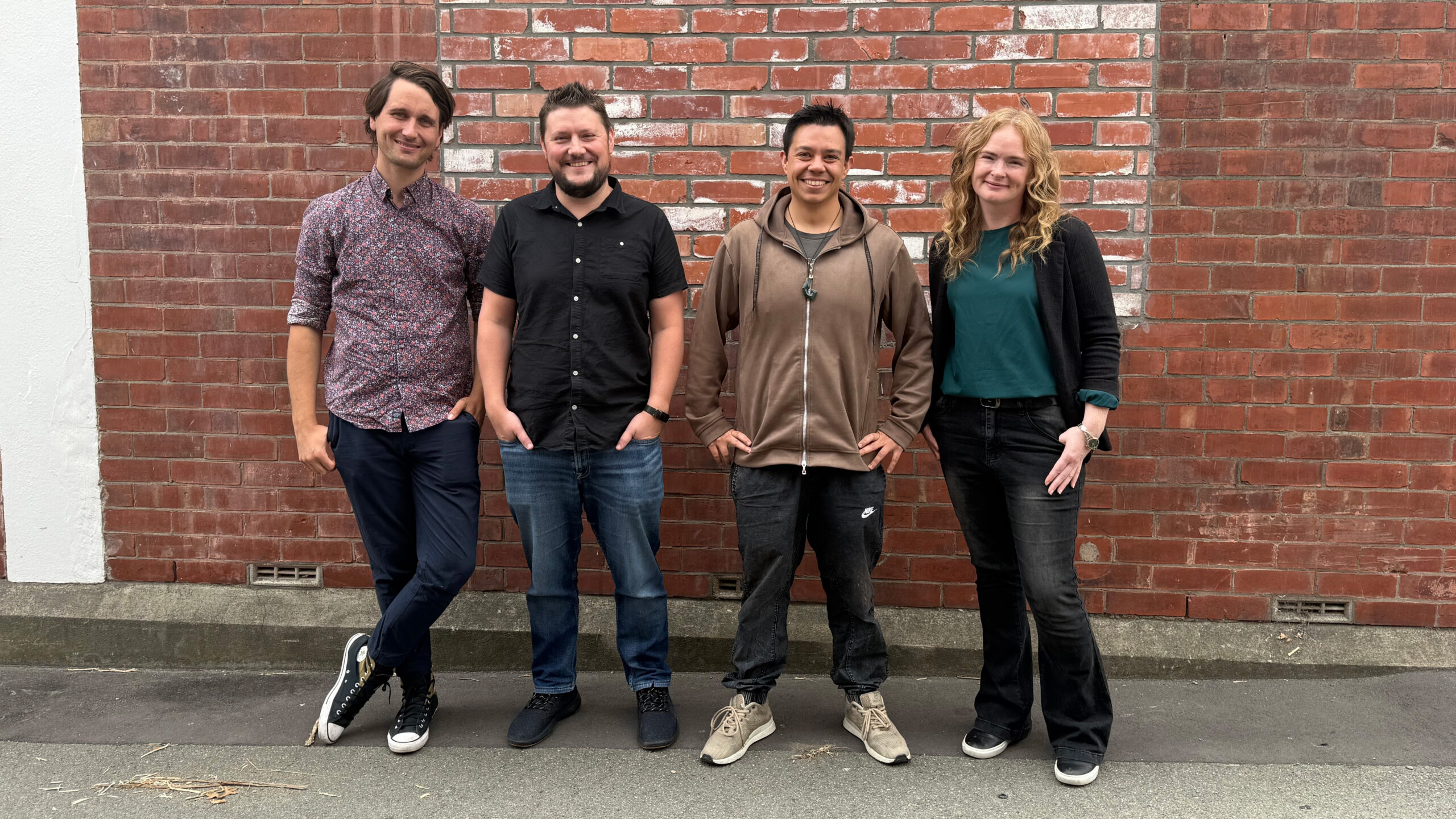 A photo of Disc 2 Games team members Kris, Nadia, Michael, and Johannes standing in front of a brick wall.
